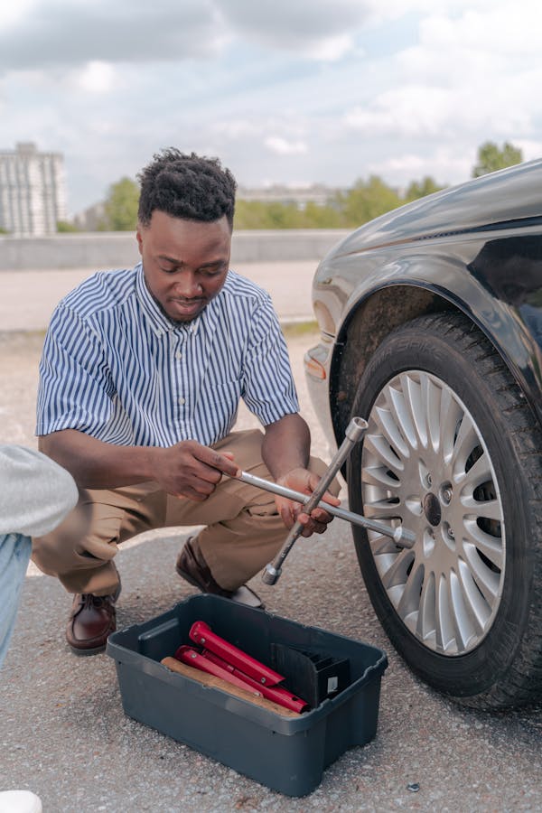 Person using a lug wrench to fully remove lug nuts from a raised car wheel
